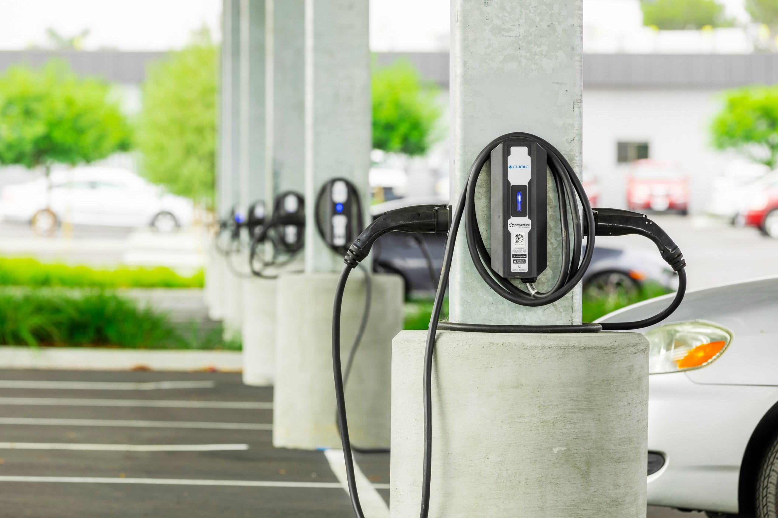 Row of electric vehicle charging stations mounted on concrete pillars in a parking lot.