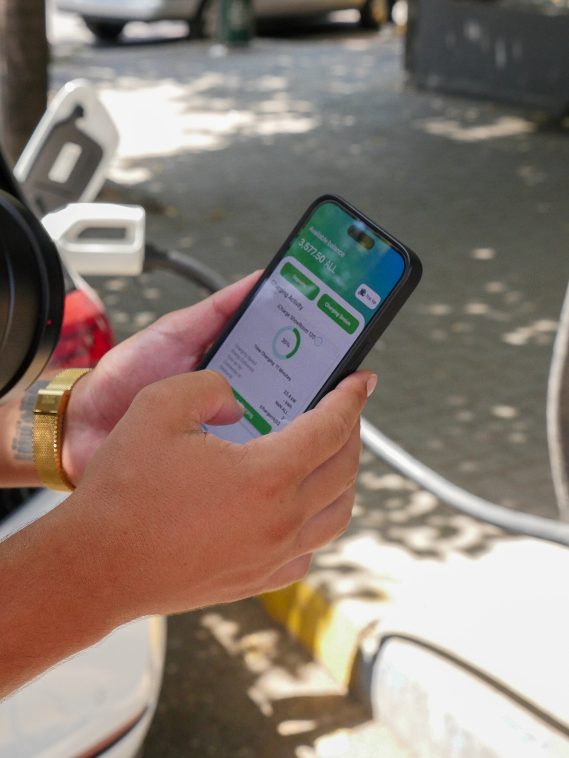 Person holding a smartphone displaying a charge activity app while charging an electric vehicle.