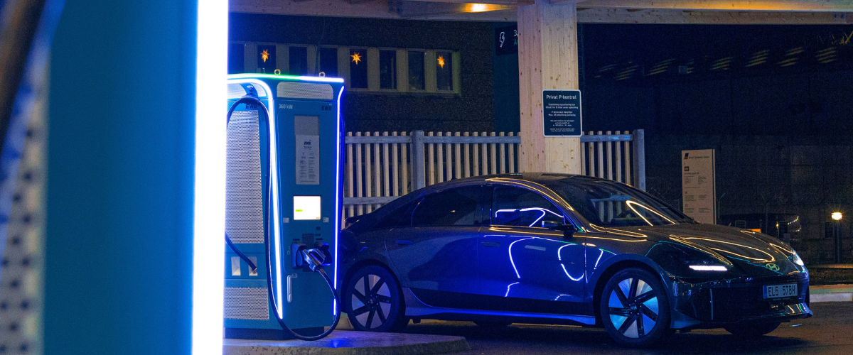Black electric car parked and charging at a blue illuminated EV charging station at night.