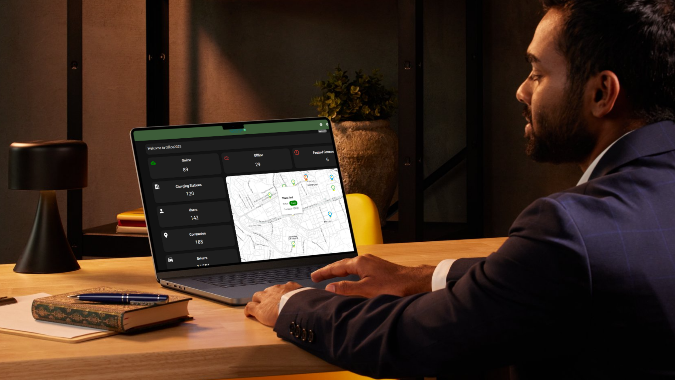 Man in a suit sitting at a desk using a laptop displaying a dashboard with map and statistics.