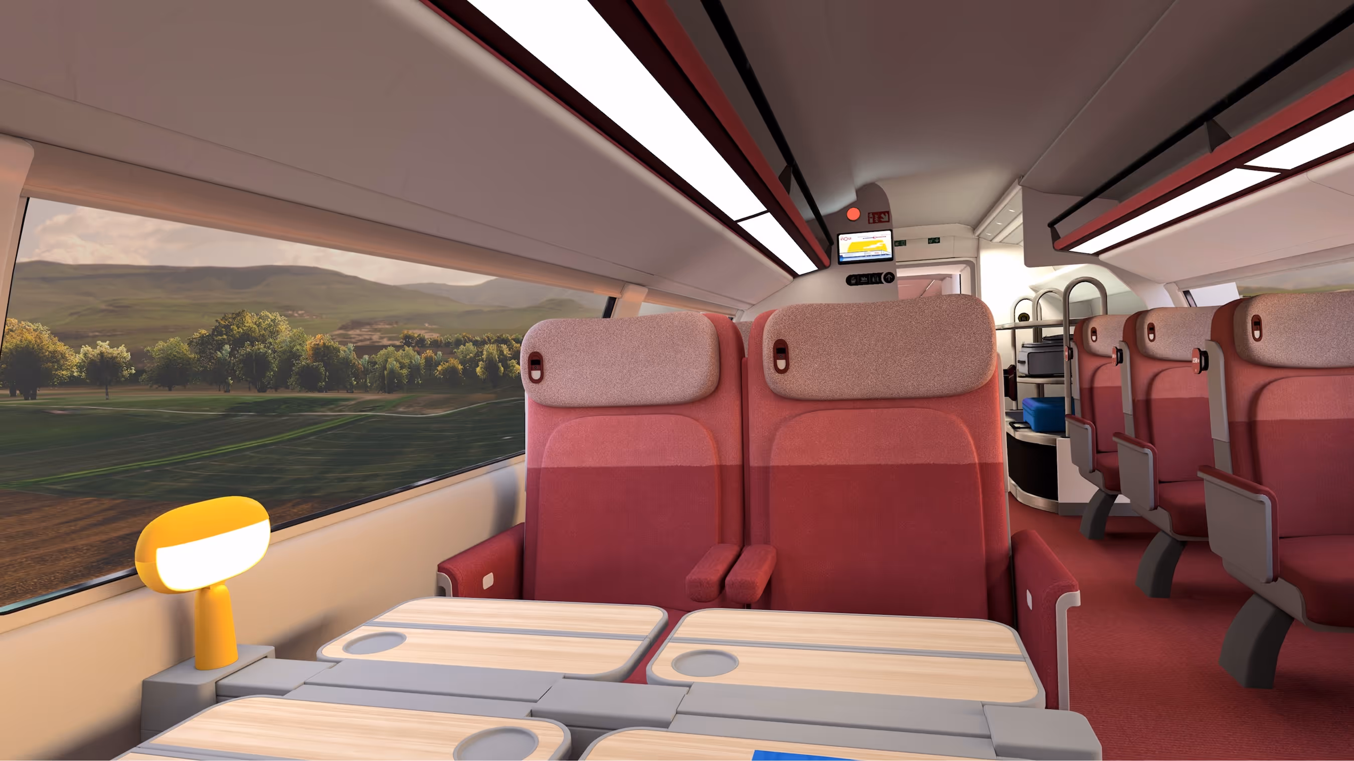 Interior of a modern train carriage with red and pink seats, foldable tables, a small yellow lamp, and a view of green fields and hills outside the window.