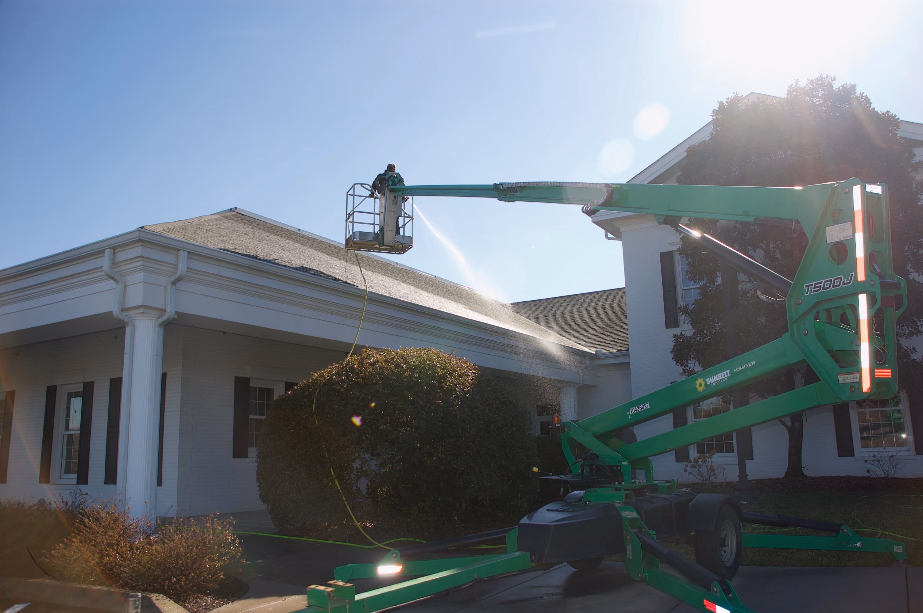 Worker in a boom lift sprays water onto a white building's gutters