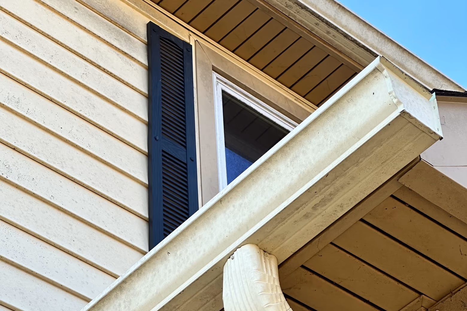 A dirty white gutter system under a wooden soffit.