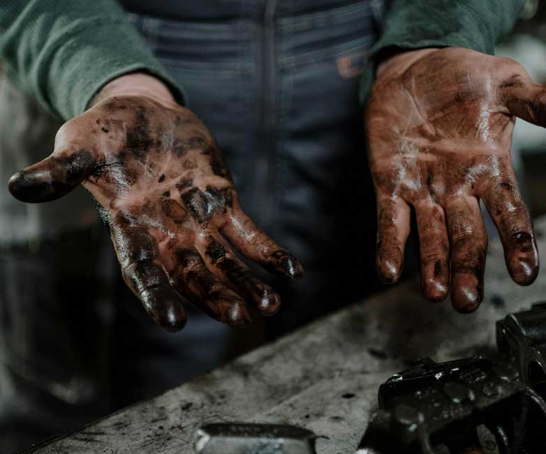 Close-up of a person's hands covered in grease and dirt, held open above a workbench with tools.