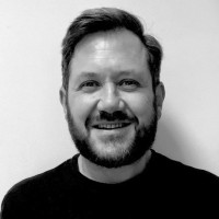 Black and white portrait of a smiling man with short hair and a beard wearing a dark shirt.