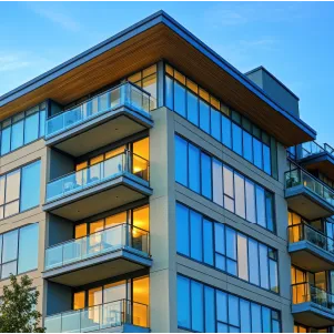 Modern apartment building with glass balconies and illuminated windows at dusk.