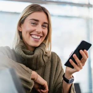 Smiling woman in a green sweater holding a smartphone indoors.