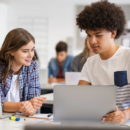 Two students collaborating and looking at a laptop in a classroom setting.