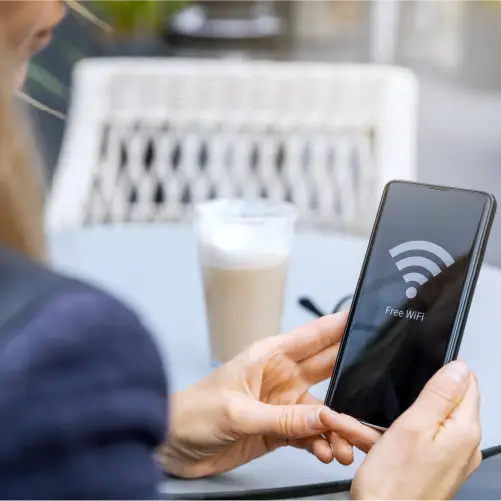 Person holding a smartphone displaying a 'Free WiFi' symbol while sitting outdoors with a latte in the background.