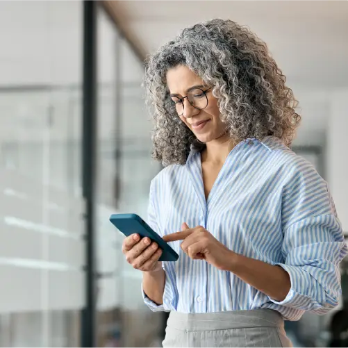 Middle-aged woman with curly gray hair and glasses using a smartphone indoors.