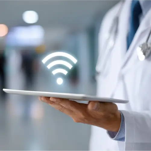 Close-up of a doctor holding a tablet with a glowing Wi-Fi symbol above it in a hospital corridor.
