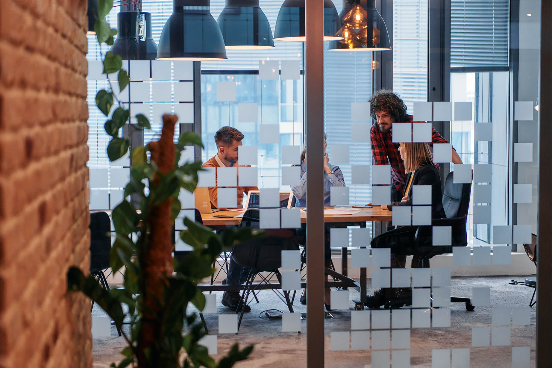 Coworkers collaborate around a wooden table in a modern office space with glass walls and plants.