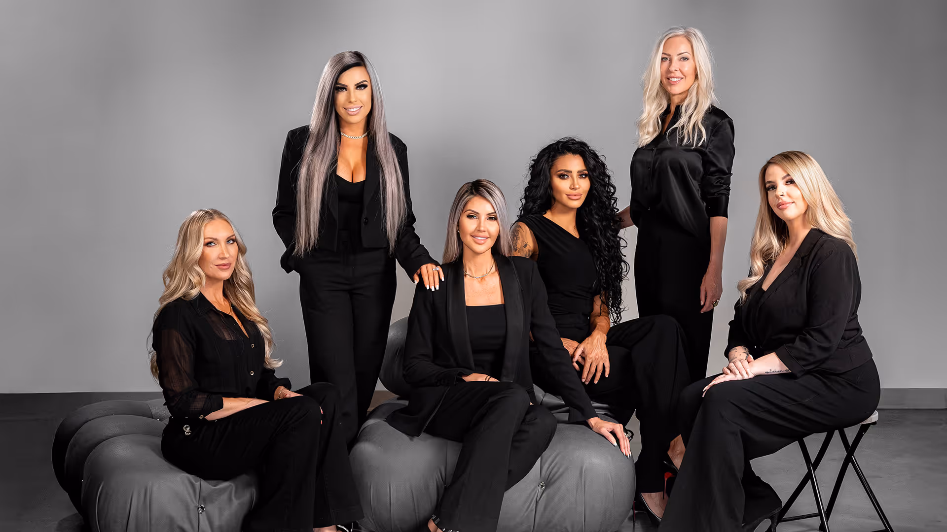Group portrait of six women dressed in black posing in a studio with professional lighting equipment.