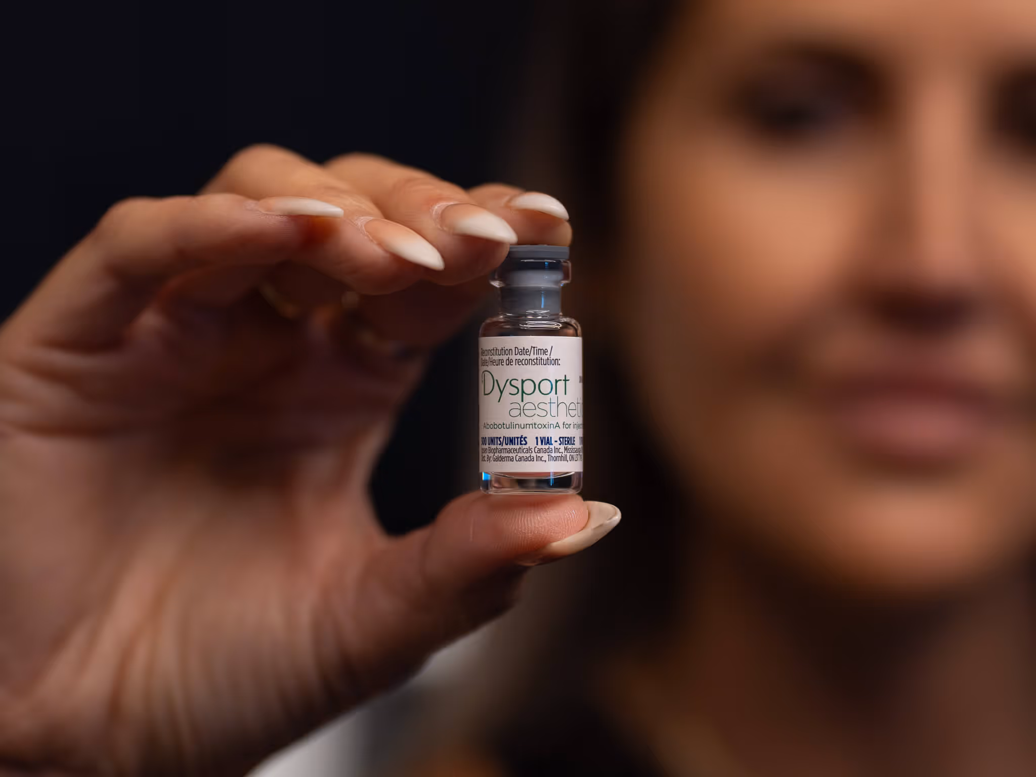 Close-up of a woman holding a small vial labeled Dysport aesthetic.