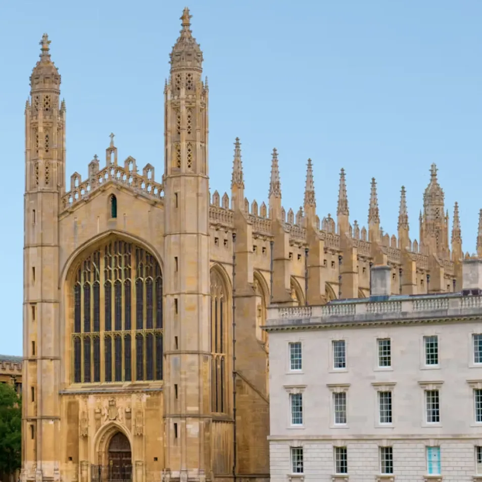 Large historic Gothic-style chapel with tall spires next to a white multi-windowed building.