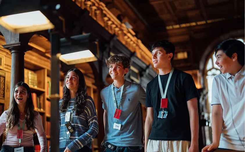 Group of five young people smiling and talking inside a wood-paneled room with bookshelves.