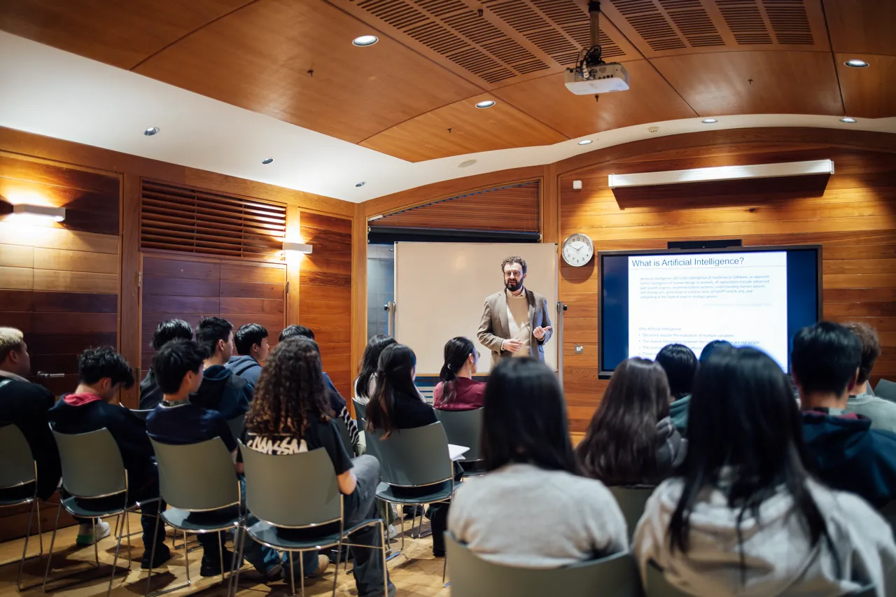 Man giving lecture on artificial intelligence to seated and attentive students in a wood-paneled room.