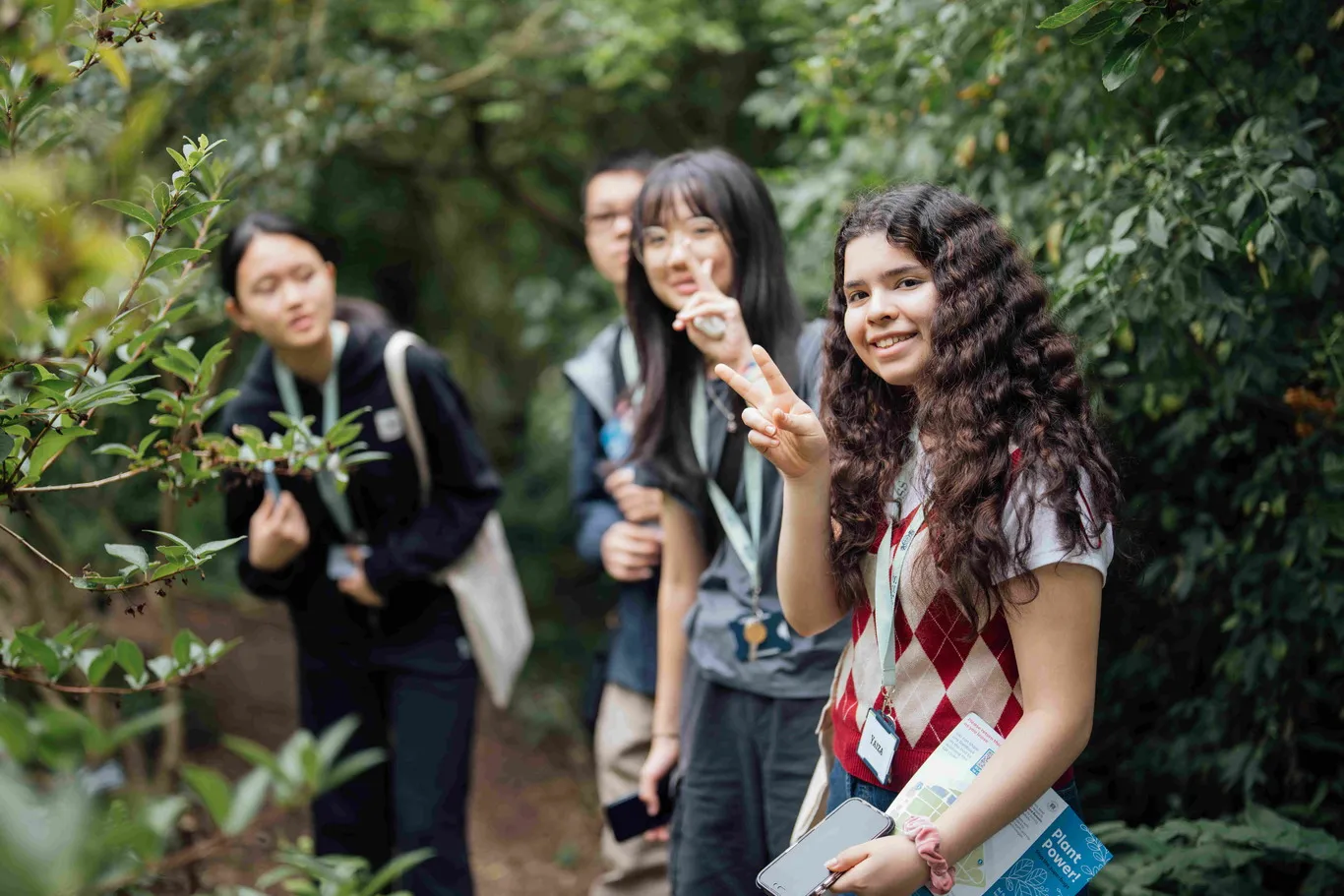 Smiling girl showing peace sign holds map during outdoor group nature walk.