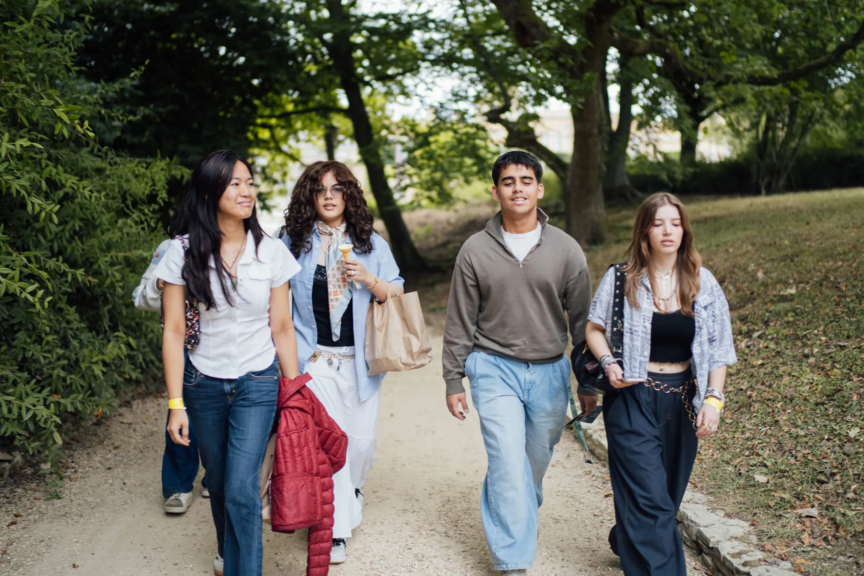 Group of four young adults walking on a park path surrounded by trees and grass.