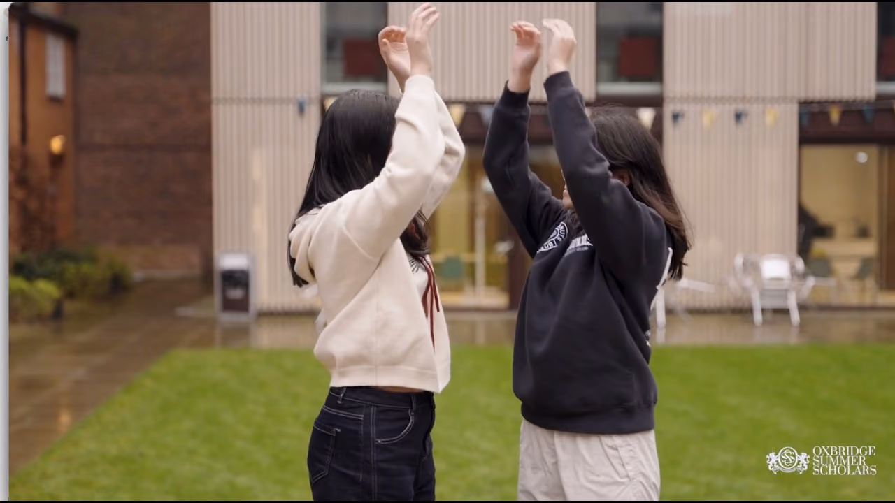 Two young women facing each other outdoors, raising their hands as if to high-five.