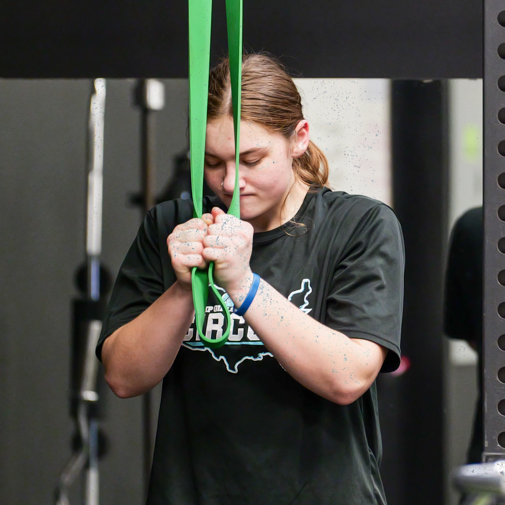 Woman in black shirt pulling green resistance band during workout at gym.