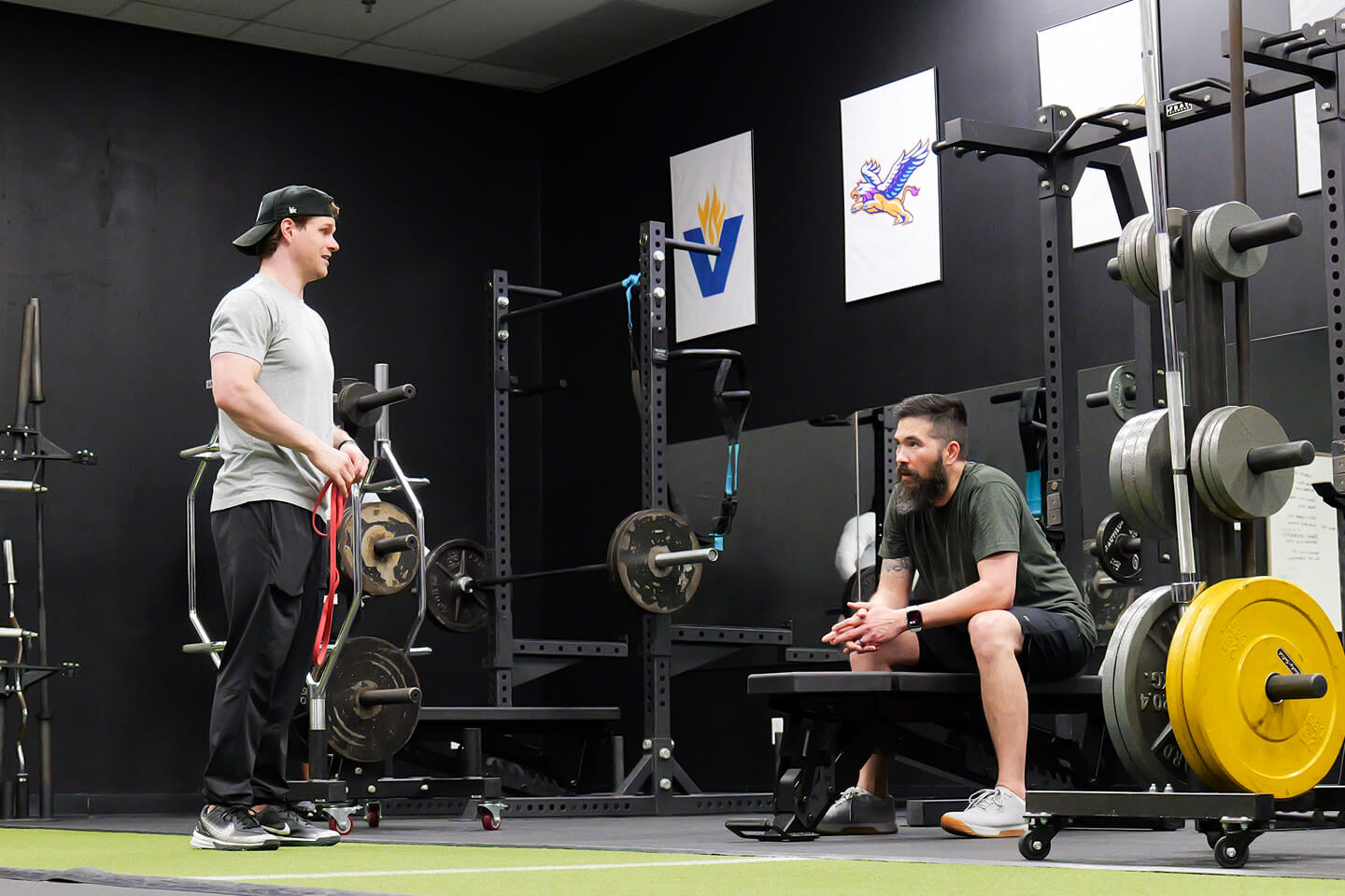 Two men in gym with weight training equipment and colorful wall posters