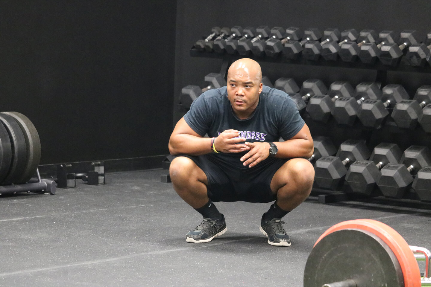 Athlete crouching in gym with dumbbells and barbell in background