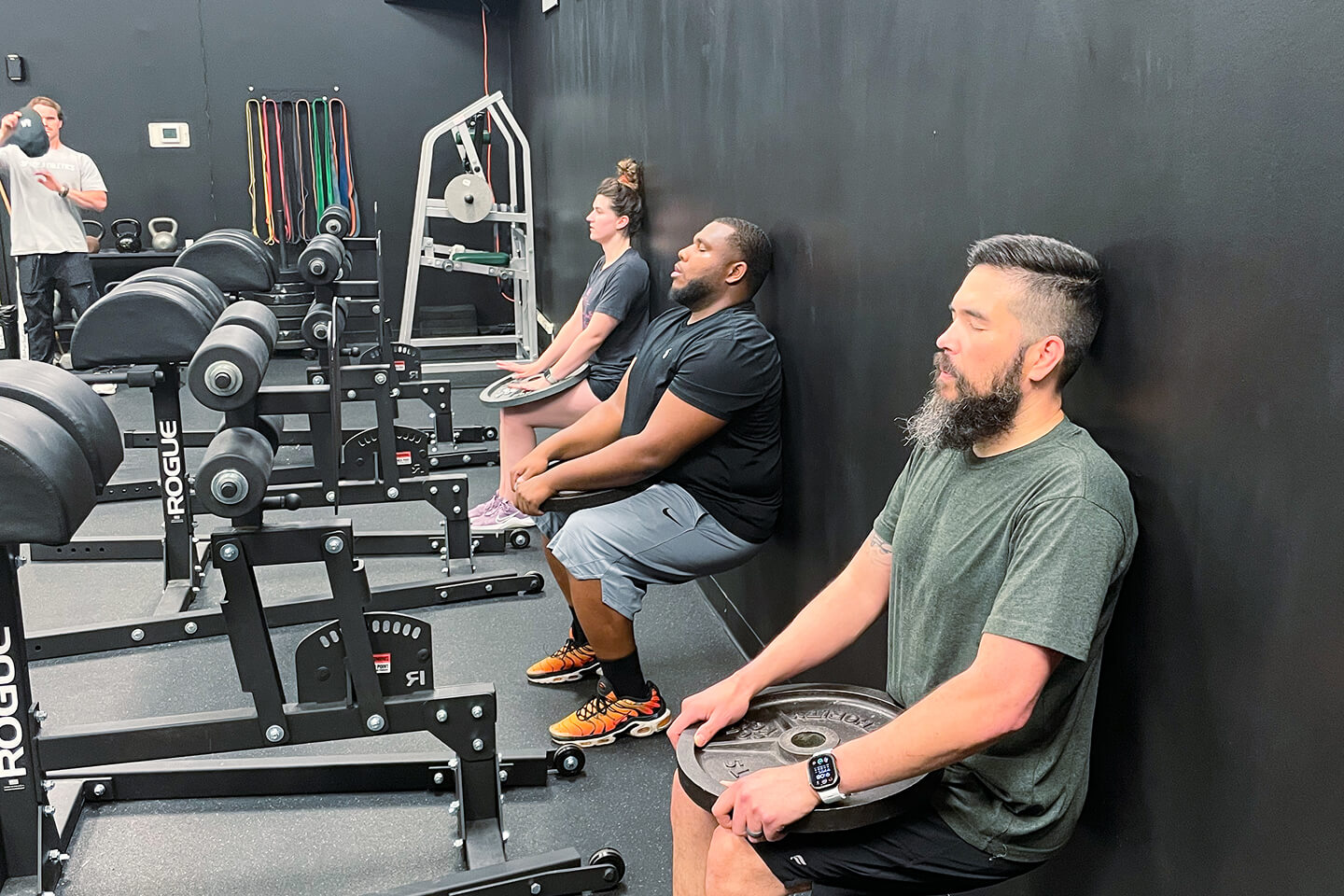 Three people resting between sets at a gym with weight training equipment