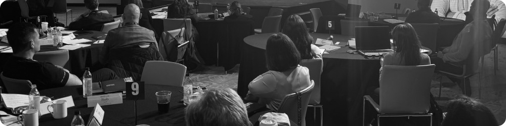 Group of people seated around conference tables attending a meeting or seminar.