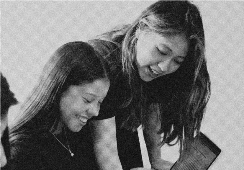Two young women smiling and looking at a laptop screen together.