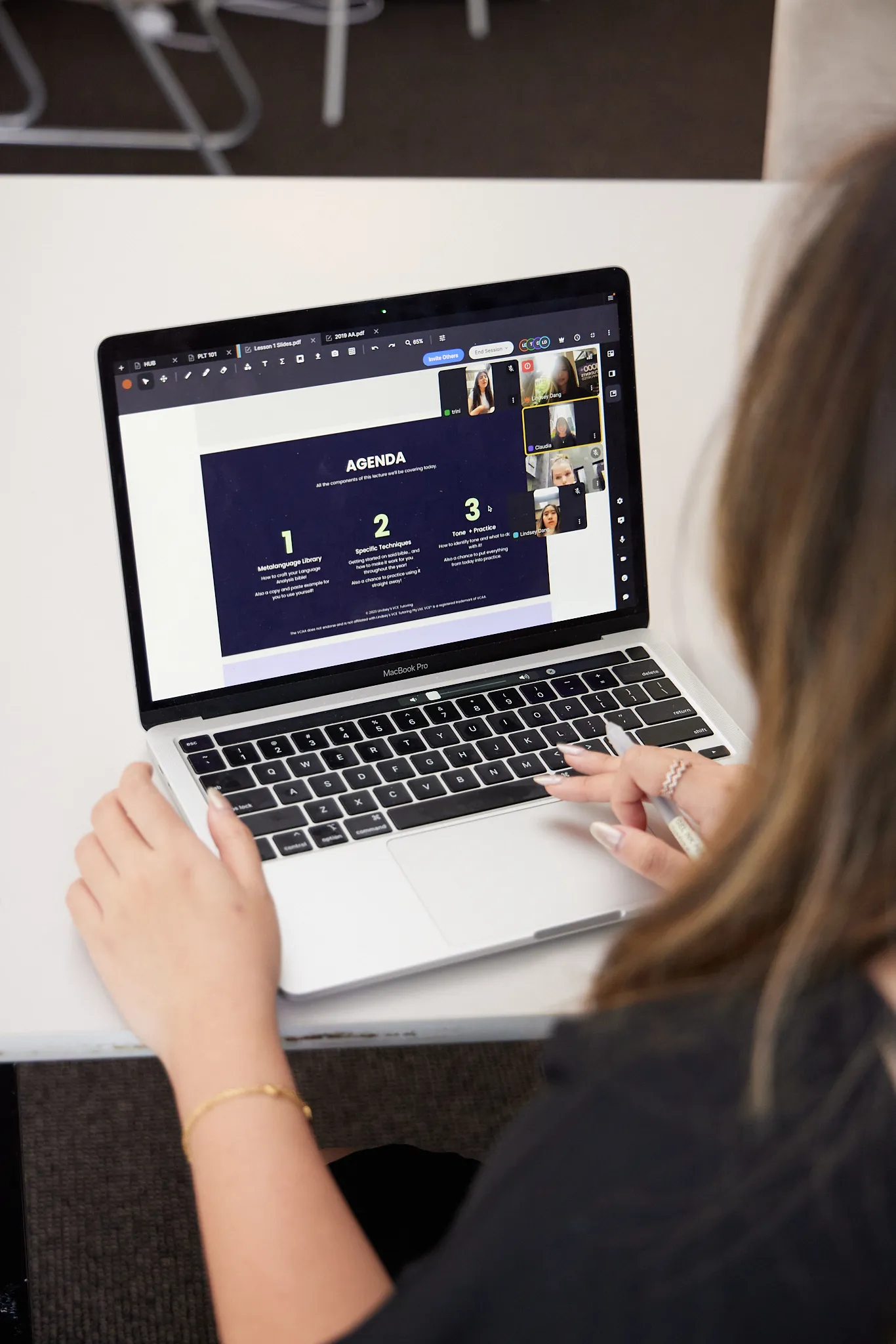 Person attending a virtual meeting on a MacBook Pro with an agenda slide and four participants visible on screen.