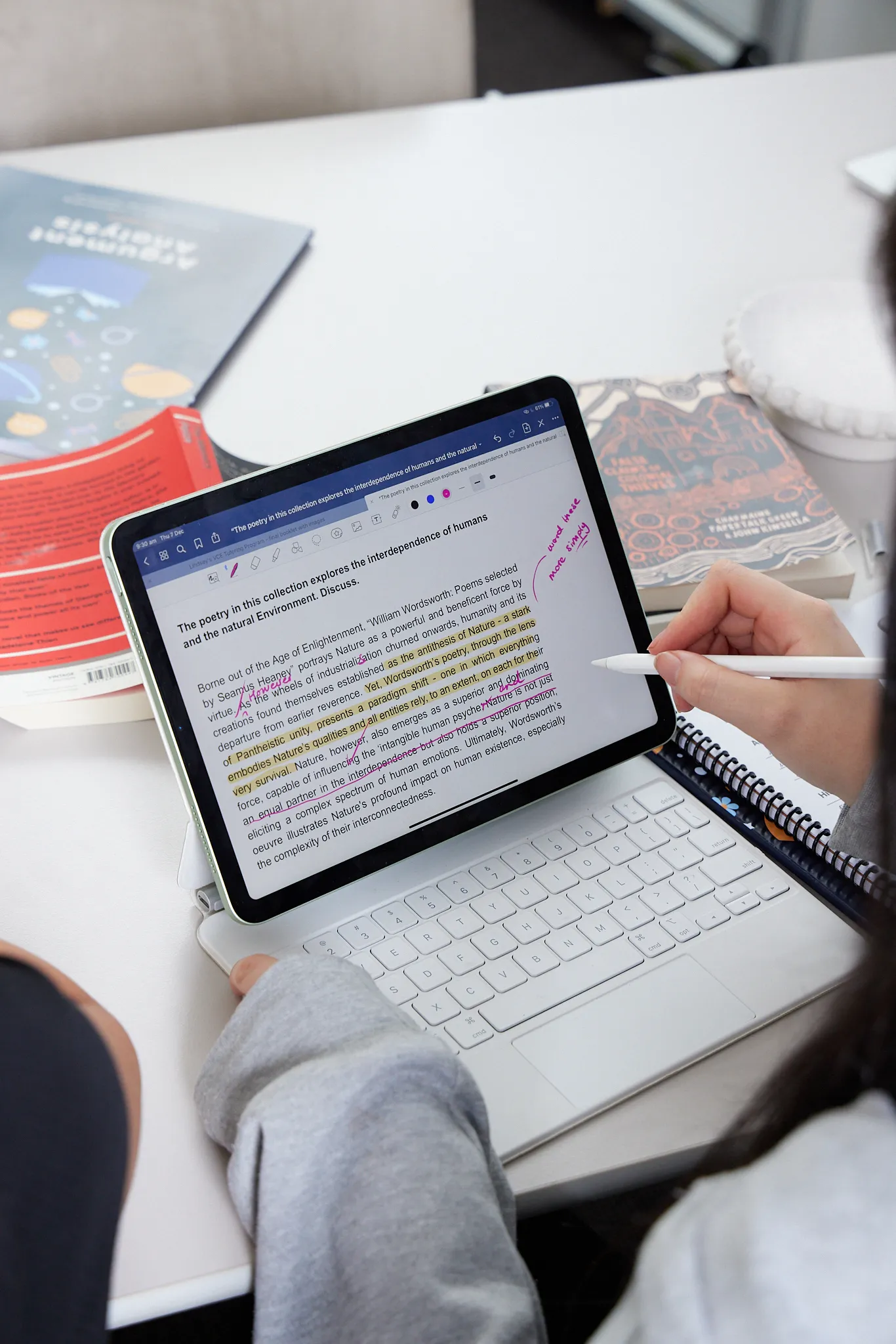 Person using a stylus to annotate a digital document on a tablet with a white keyboard, with highlighted and handwritten notes visible.