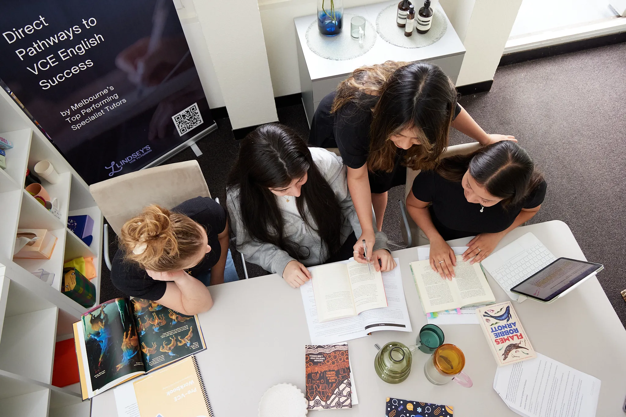 Four students gathered around a table studying together with books, papers, and a tablet.