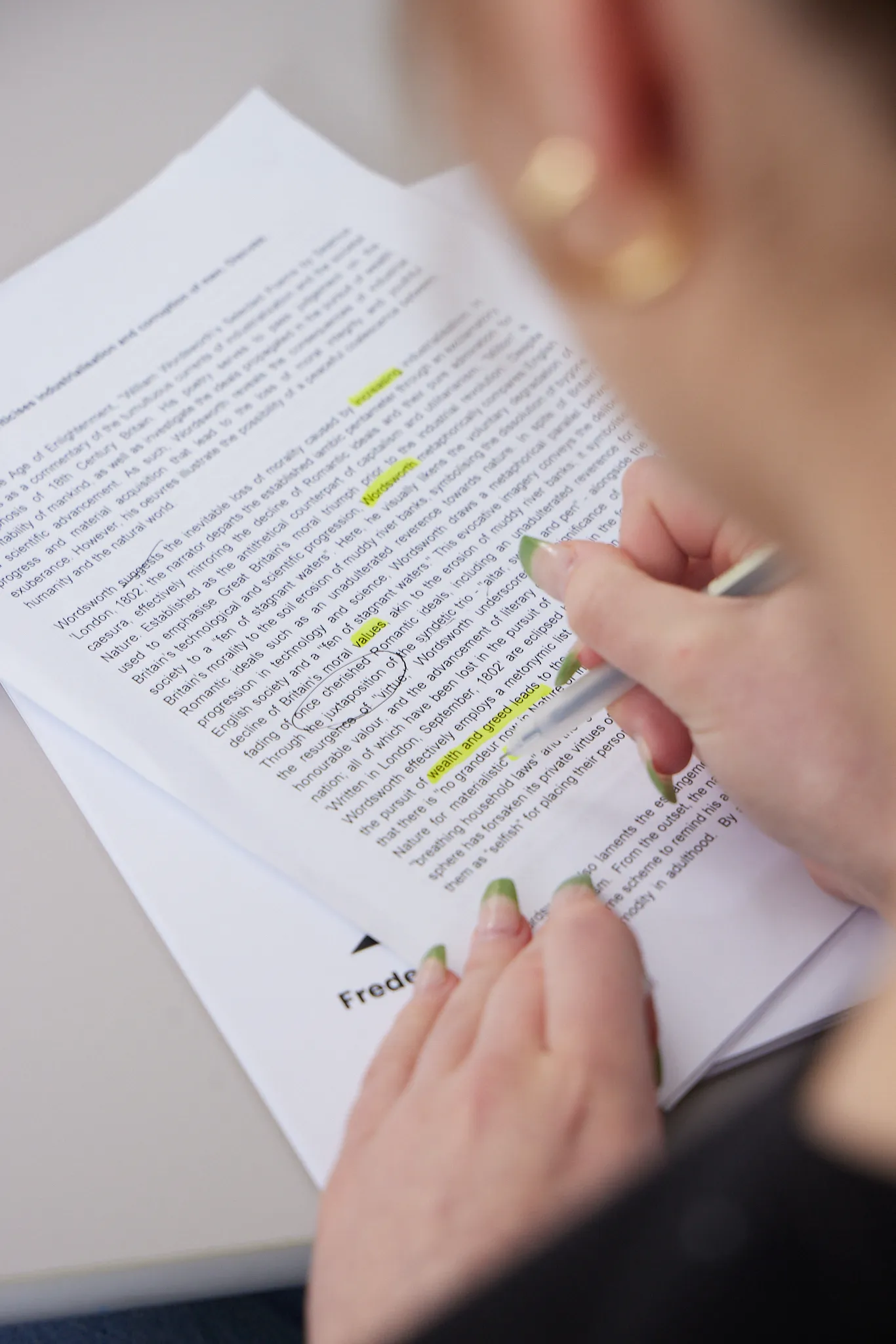 Person with green-tipped nails highlighting text on a printed document using a silver pen.