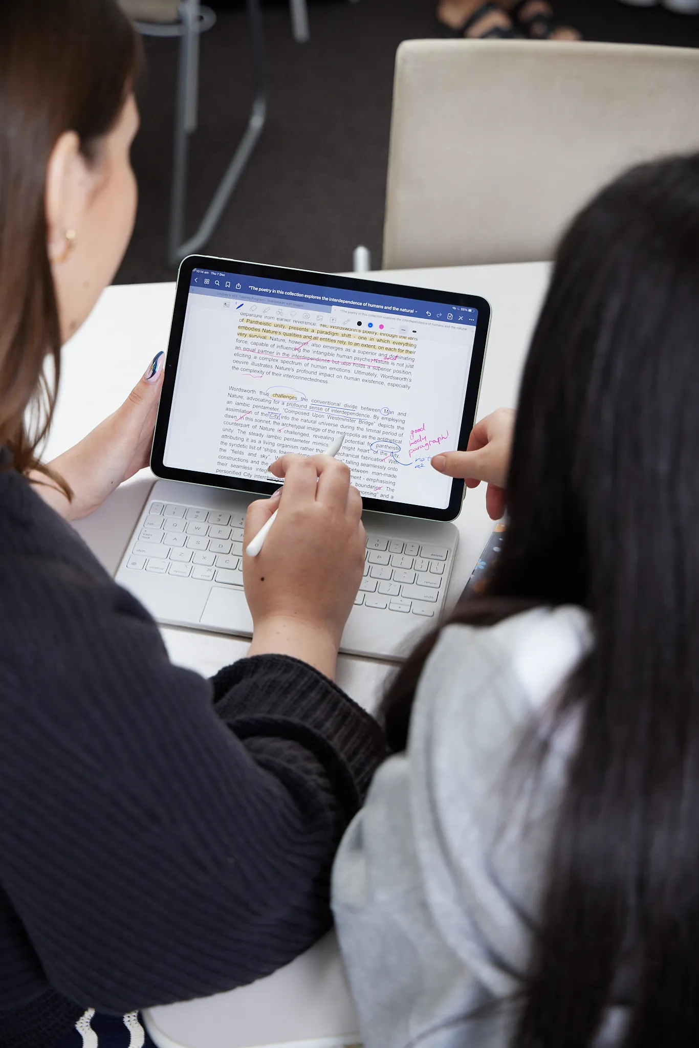 Two people reviewing and annotating a text document on a tablet with a stylus at a white desk.