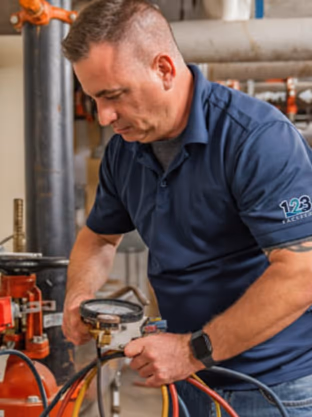 Technician in a blue shirt adjusting gauges on HVAC equipment connected to colored hoses.