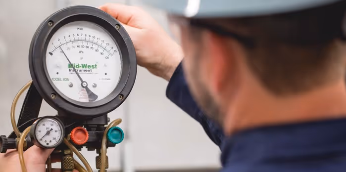 A technician wearing a helmet adjusts a pressure gauge on industrial equipment.