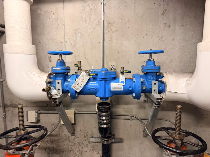 Blue backflow preventer with insulation against a concrete wall.
