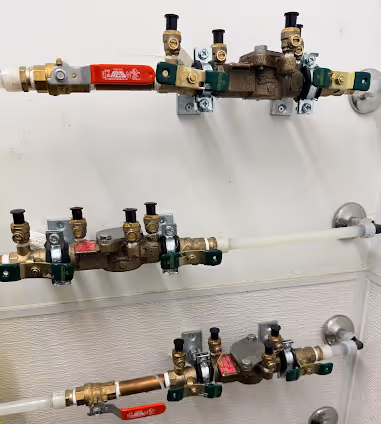 Wall-mounted plumbing manifolds with multiple valves and red-handled shut-off levers connected to pipes.