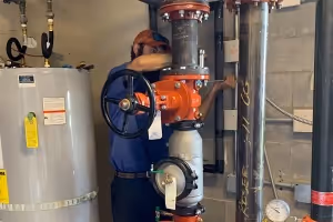 Technician in blue uniform working on large red valve connected to industrial pipes.