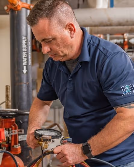 Technician in blue polo working on a water supply gauge in an industrial setting.
