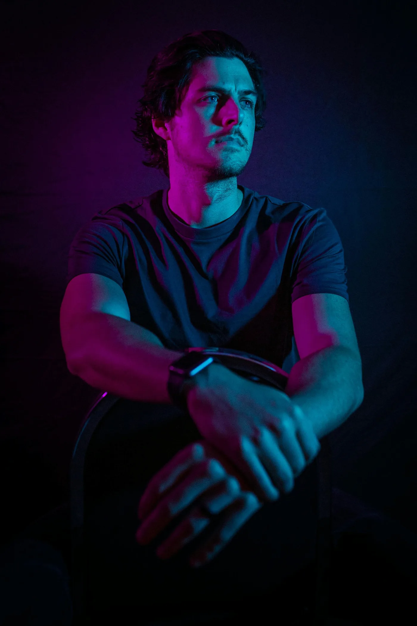 Portrait of a man with crossed arms, lit in pink and blue studio light.