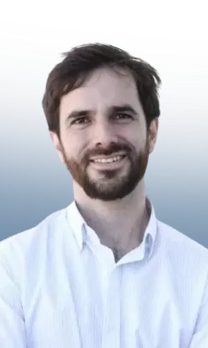 Hombre joven con barba y cabello oscuro sonriendo, vistiendo camisa blanca, fondo azul degradado.