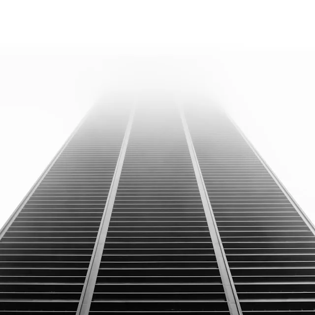Perspectiva desde abajo de un rascacielos con ventanas horizontales que se desvanece en la niebla en la parte superior.