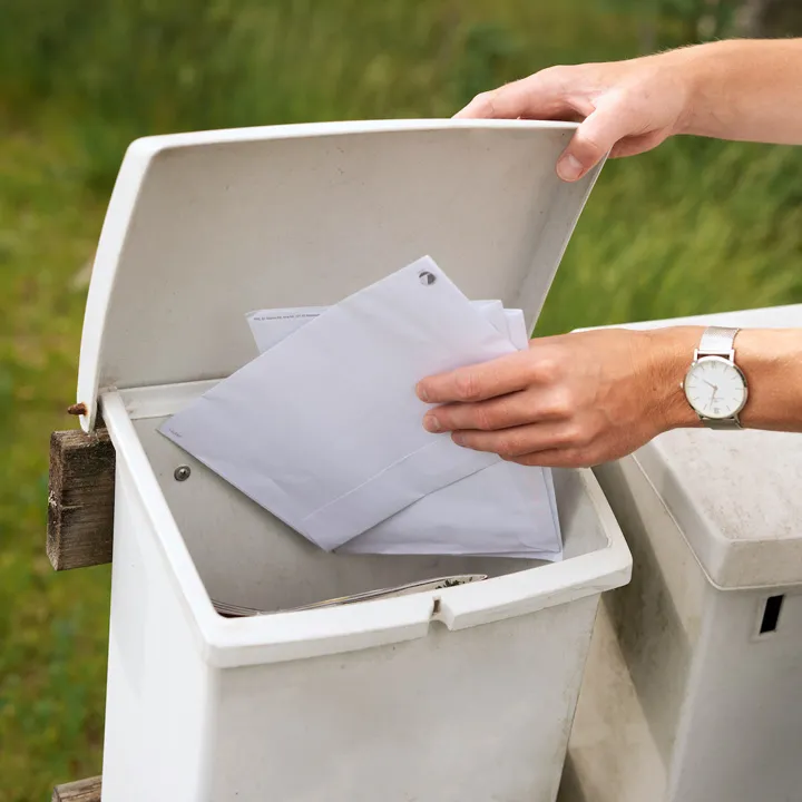 Två händer öppnar en brevlåda och lägger in ett par förseglade brev i den.
