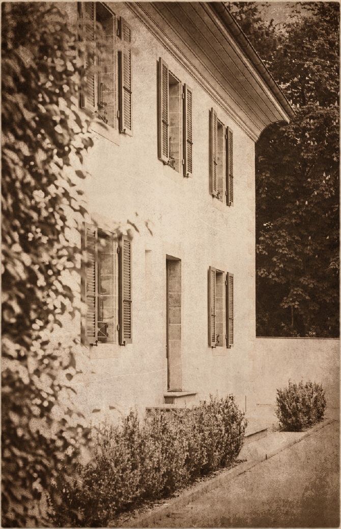 Sepia-toned image of a building wall with several closed window shutters and bushes along a pathway.
