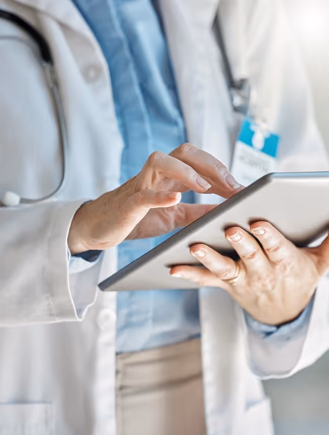 Healthcare professional in white coat using a digital tablet.
