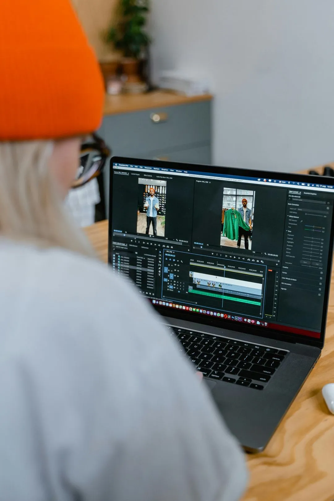 Person wearing an orange beanie and glasses editing a video of a man holding a green shirt on a laptop.