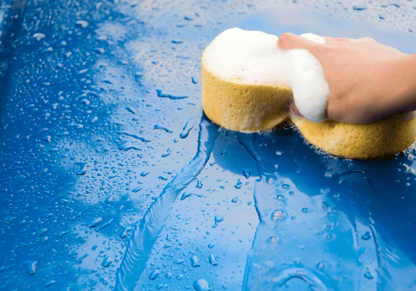 Blaues Fahrzeug wird mit einem Schwamm gewaschen.