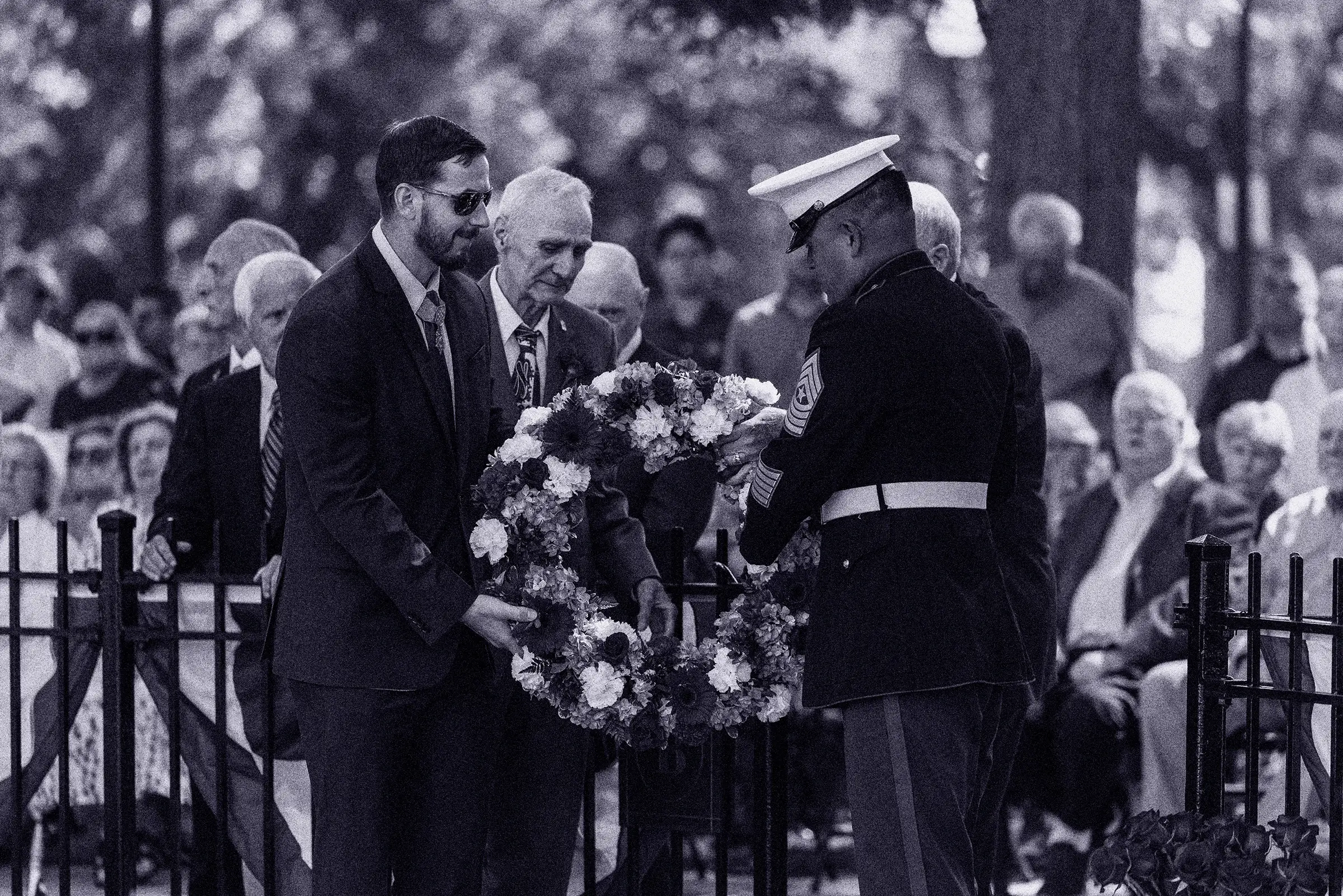 A man in a suit is placing a wreath on a black metal fence.